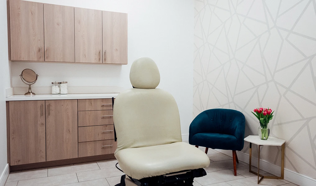 Modern medical exam room with beige patient chair, blue seating, wooden cabinets and geometric wall design