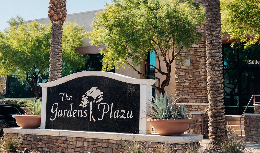 Gardens Plaza entrance sign with palm trees and landscaping in upscale residential community