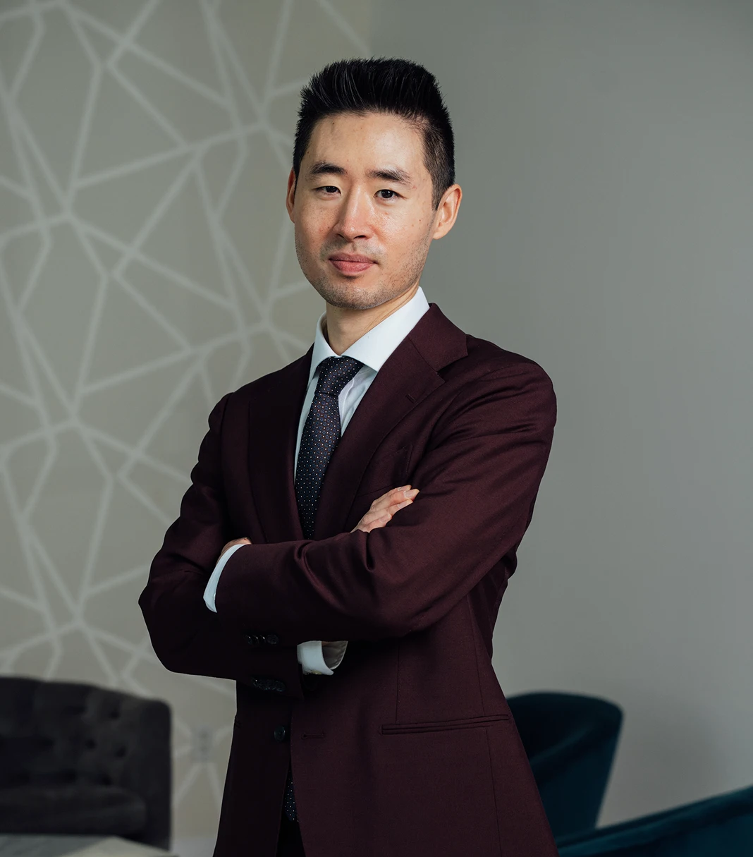 Professional surgeon in burgundy suit with arms crossed standing in modern medical office