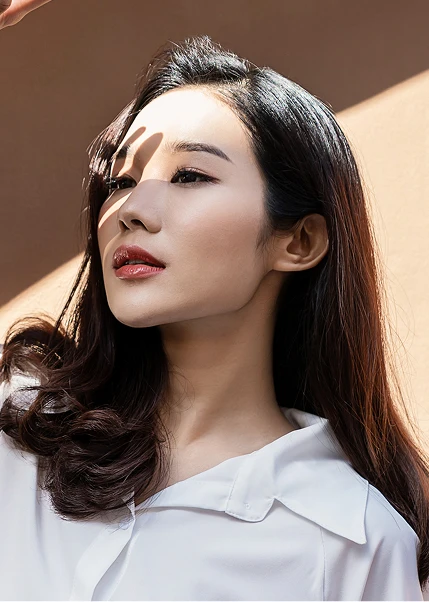 Asian woman with long dark hair and white collar shirt looking upward in natural sunlight