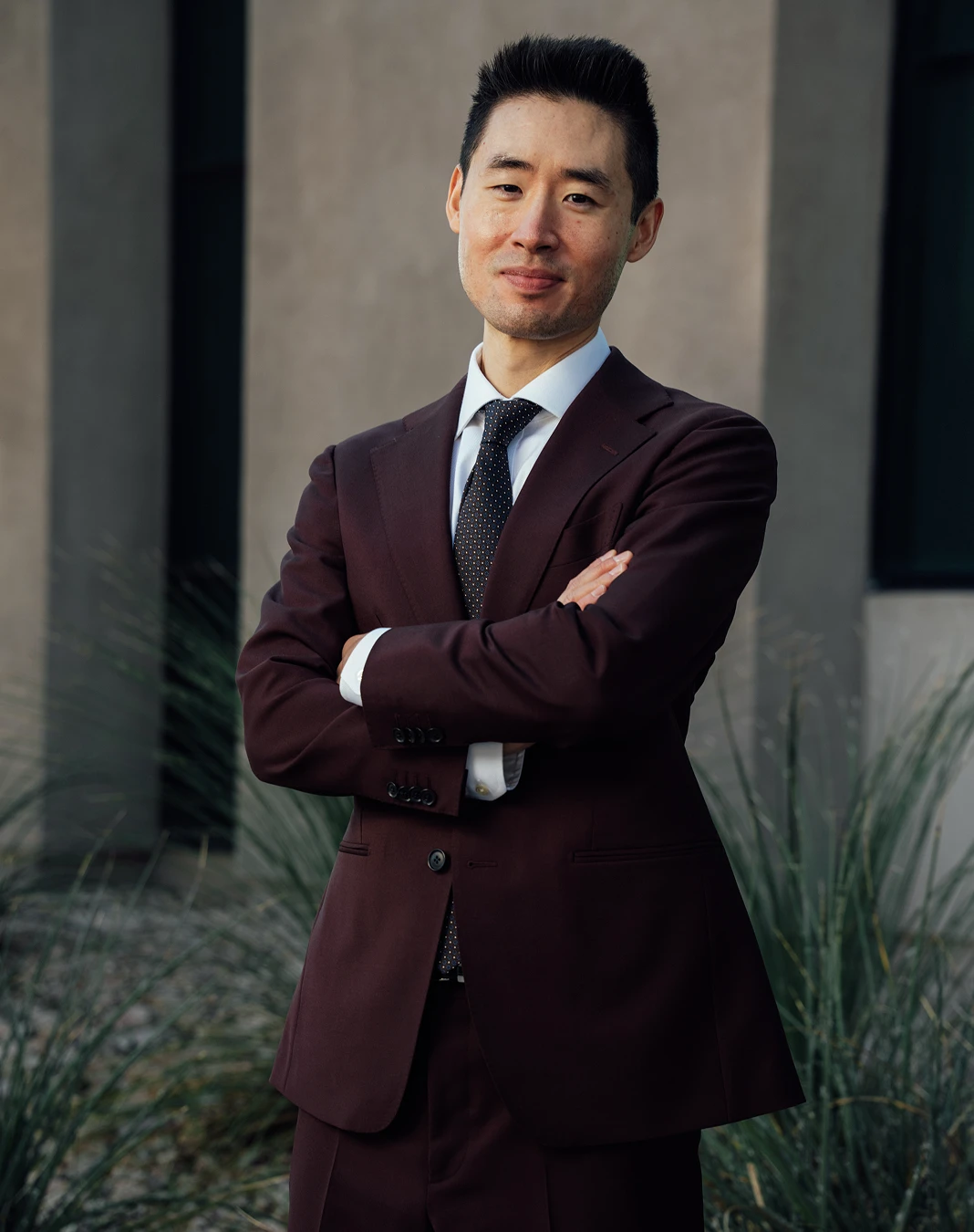 Harry Ching MD in burgundy suit with arms crossed standing confidently in modern office setting