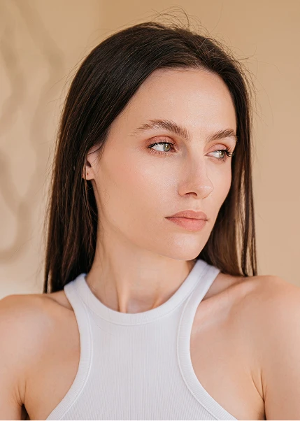 Young woman with long dark hair wearing white sleeveless top against neutral beige background