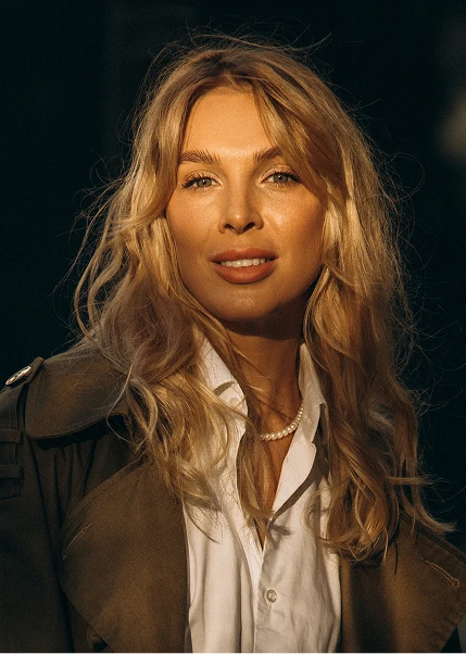 Woman with long blonde wavy hair wearing white shirt and dark jacket in golden hour lighting