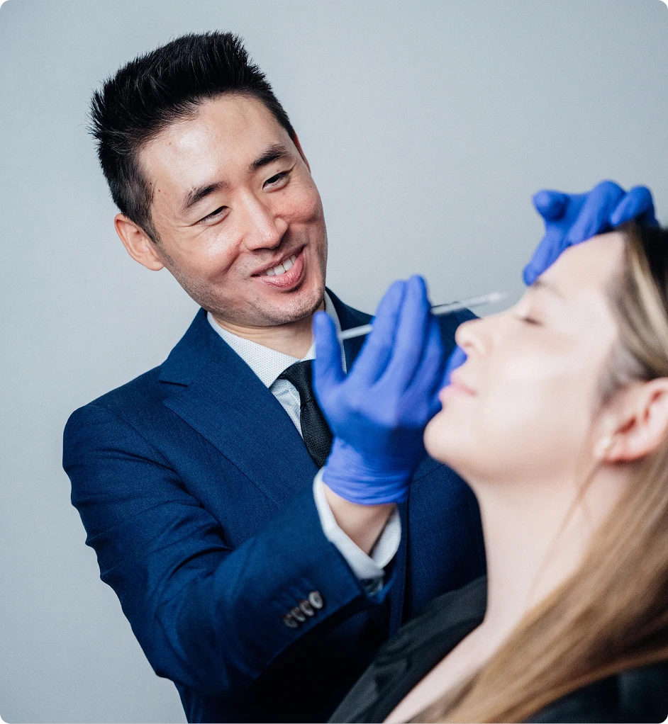Harry Ching MD in blue suit examining female patient's face while wearing medical gloves
