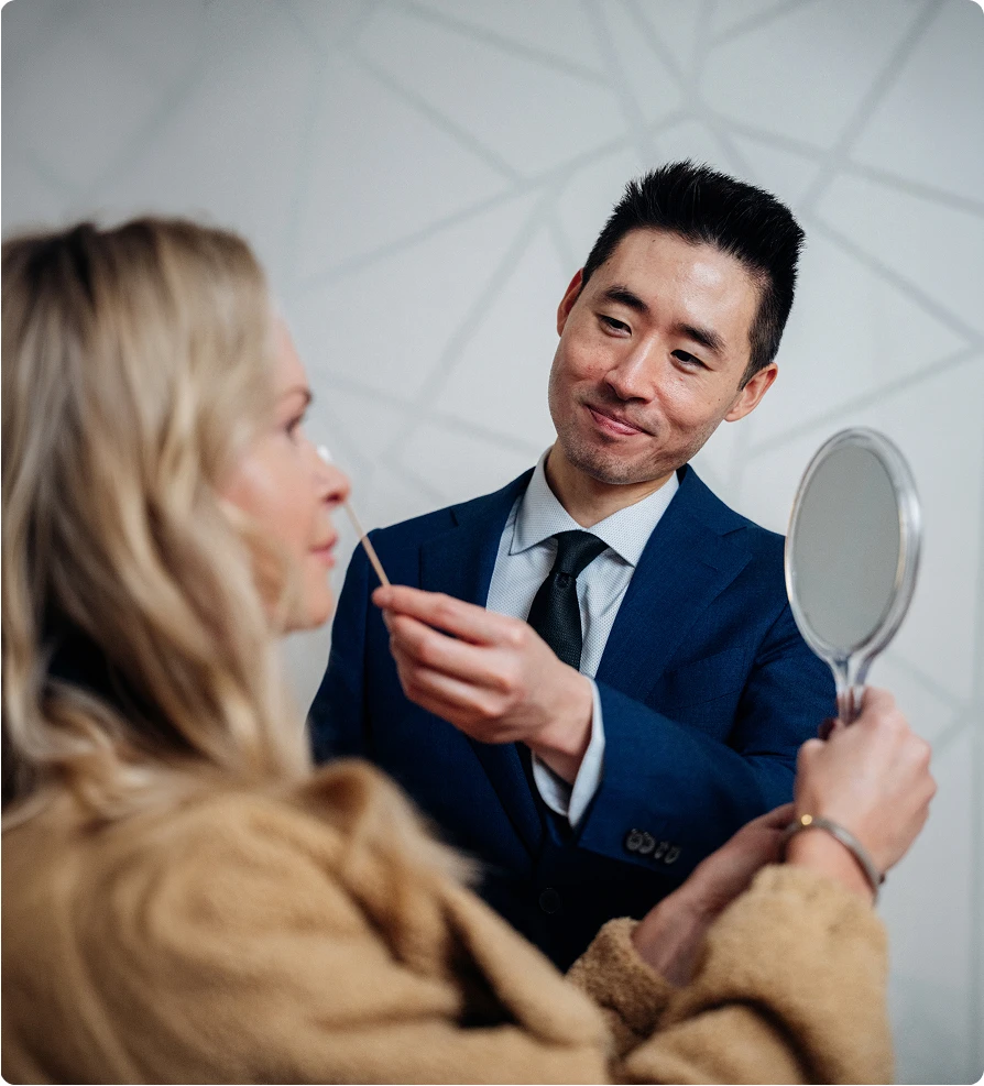 Harry Ching MD consulting with female patient while holding mirror during cosmetic procedure consultation
