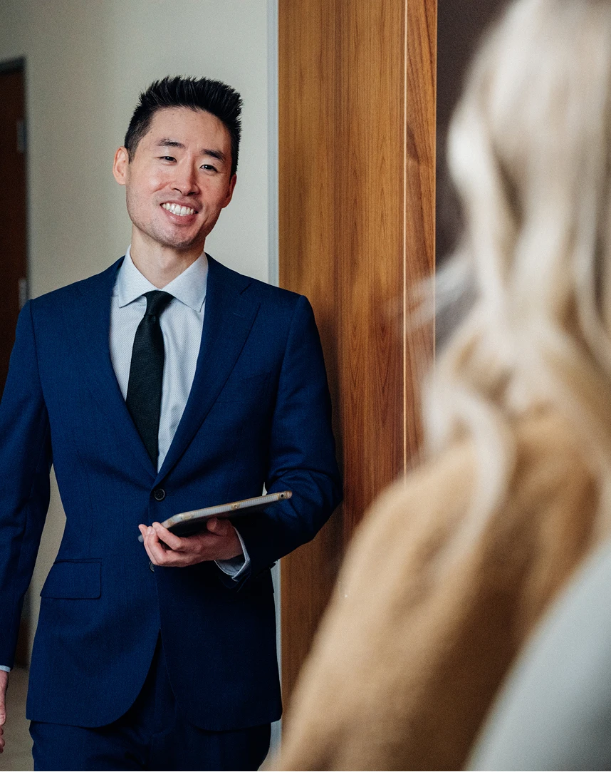 Harry Ching MD in navy suit holding tablet consulting with client in modern office setting