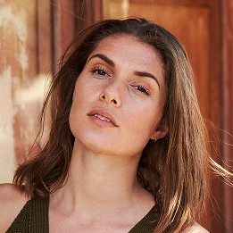 Woman with long brown hair and natural makeup looking at camera in warm golden lighting