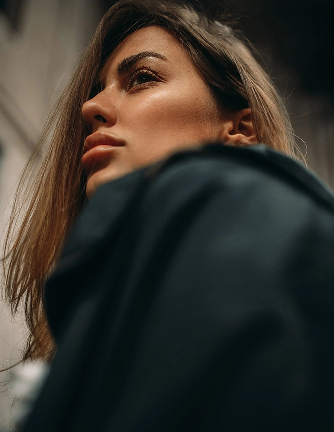 Confident woman in black coat looking upward with dramatic lighting and soft focus background - Brow Lift in Las Vegas, NV