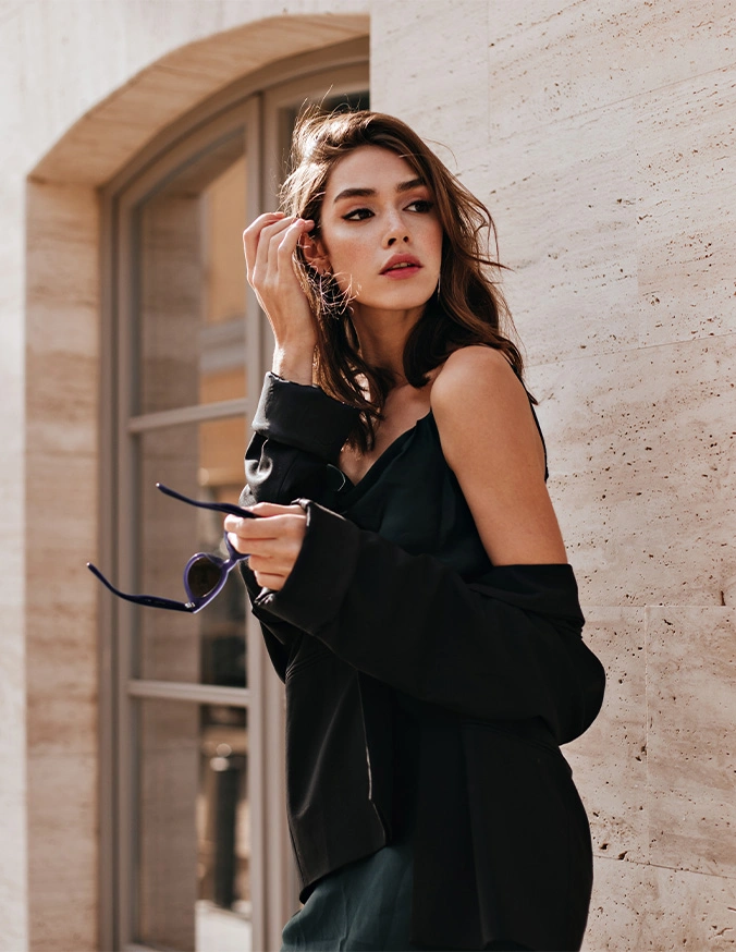 Elegant woman in black off-shoulder outfit posing by textured wall with arched window background - Buccal Fat Removal in Las Vegas, NV