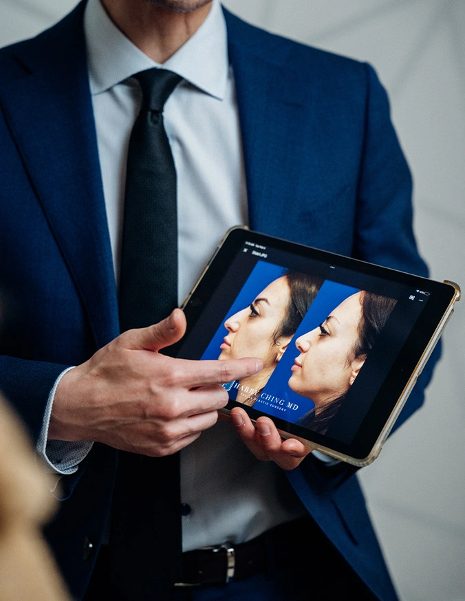 Harry Ching MD in navy suit holding tablet displaying dental X-ray images during patient consultation - Ethnic Rhinoplasty in Las Vegas, NV