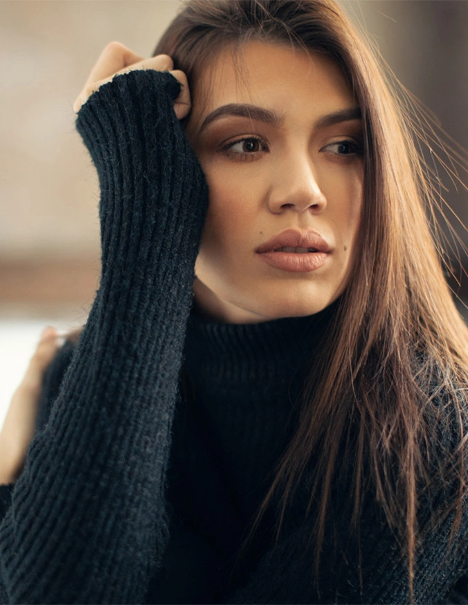 Woman in black turtleneck sweater with long dark hair resting hand on head in contemplative pose - Eyelid Surgery in Las Vegas, NV