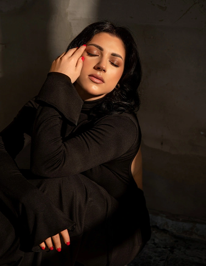 Woman in black turtleneck posing with hand near face in dramatic golden lighting against dark background - Facial Implants in Las Vegas, NV