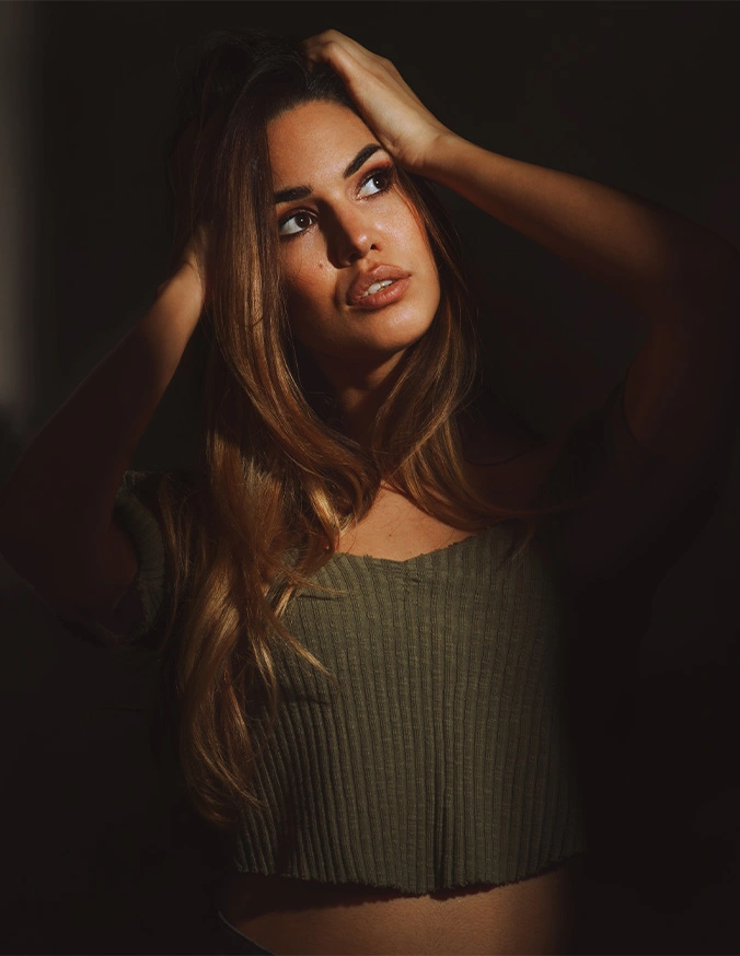 Woman with long brown hair in olive green top posing with hand in hair against dark background - Laser Resurfacing C02 in Las Vegas, NV