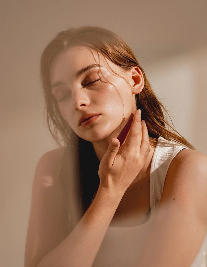 Young woman with long brown hair touching her neck in soft natural lighting, beauty portrait - Otoplasty in Las Vegas, NV