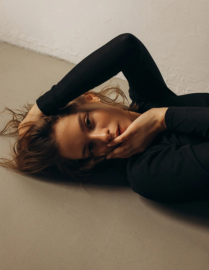 Woman in black outfit lying on white surface in contemplative pose with natural lighting - RF Microneedling in Las Vegas, NV